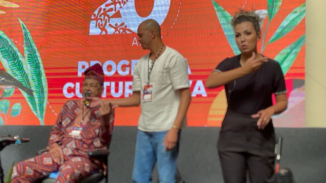 Interpretação de Libras em evento cultural com idoso convidado no palco